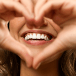 Caucasian female making a heart with hands around a healthy smile white teeth