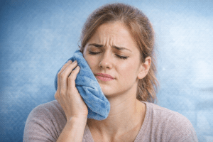 Woman holding an ice pack to the side of her face following wisdom tooth extraction